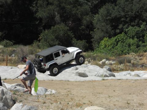 1986 Ford Bronco - A white Jeep Wrangler navigates a rocky off-road course on a sunny day.