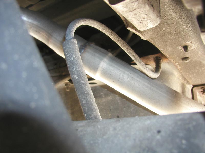 Close-up of a brake line looping down along a dusty chassis bracket under a vehicle