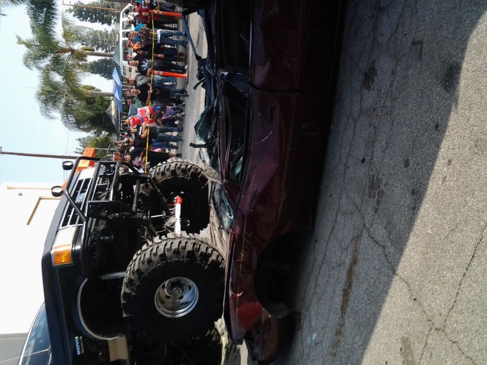 Modified truck with large tires next to a crushed red car