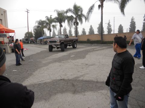 1986 Ford Bronco - A lifted pickup truck is parked in a lot with people watching.