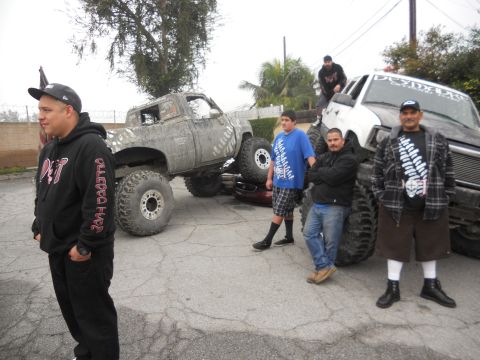 1986 Ford Bronco - Several people gather around two heavily modified trucks, one appearing to be a pickup and the other a large SUV or van.