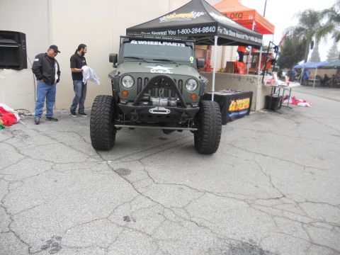 1986 Ford Bronco - Olive green Jeep Wrangler with aftermarket bumper, winch, and large off-road tires is displayed at an event.