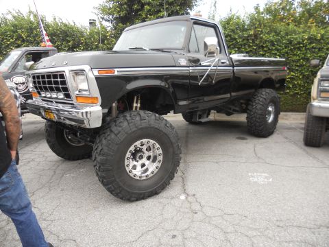 1986 Ford Bronco - This lifted black Ford pickup truck, likely from the late 1970s, is parked outdoors next to another vehicle.