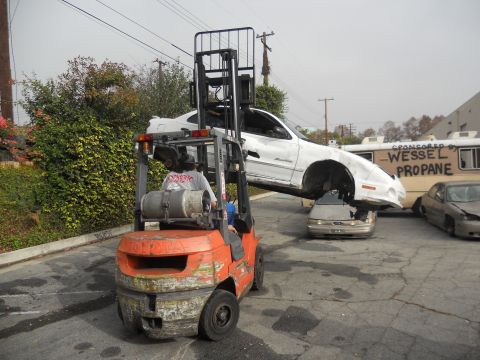 1986 Ford Bronco - A forklift lifts a white car, which is precariously balanced on top of another vehicle, in front of a Wessel Propane truck.