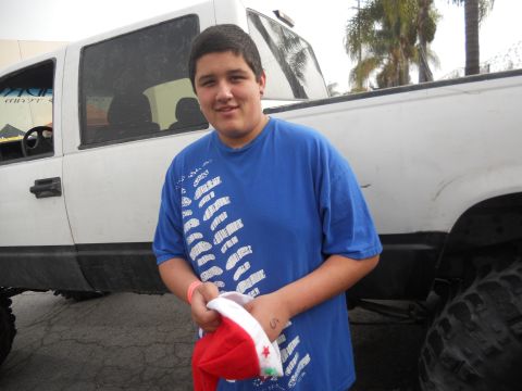1986 Ford Bronco - A young man poses in front of a lifted white pickup truck, holding a Santa hat.