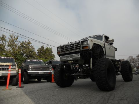 1986 Ford Bronco - A heavily modified white Ford truck with oversized tires is parked alongside other vehicles.