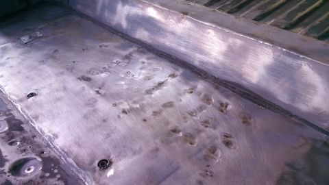 1979 Ford Bronco - The interior floor of a vehicle, showing numerous dents and bolt holes, possibly indicating past repairs or modifications.