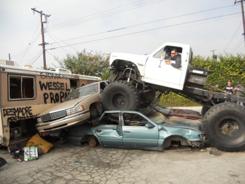 1986 Ford Bronco - Monster truck crushing multiple vehicles, including a van with graffiti.