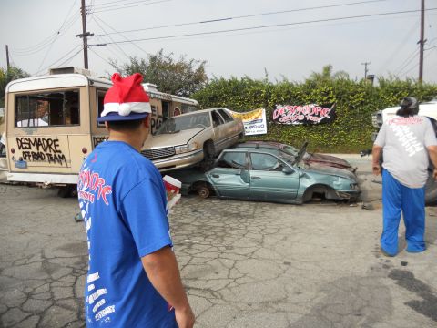 1986 Ford Bronco - A collection of damaged vehicles are piled up, with a person wearing a Santa hat in the foreground.