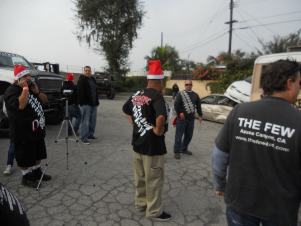 People in Santa hats stand near damaged cars, one with a white front end visible