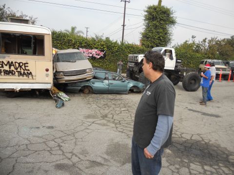 1986 Ford Bronco - A collection of damaged vehicles and a monster truck are gathered in a lot.