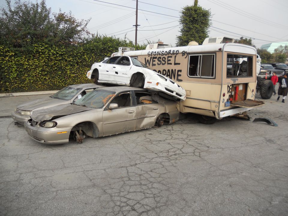Damaged cars piled up, one on top of another, next to a bus with text on its side