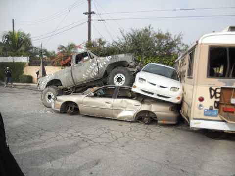 1986 Ford Bronco - A chaotic scene with multiple vehicles crushed and stacked, including a monster truck and a bus.