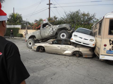 1986 Ford Bronco - A collection of damaged vehicles are stacked on a street, with a large truck crushing a sedan.