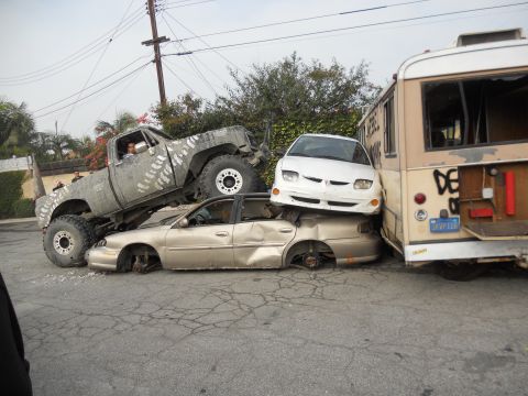 1986 Ford Bronco - A lifted pickup truck is crushing a sedan, which is also being crushed by a white car and a bus.