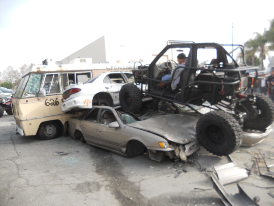Crushed cars and a van under a custom buggy, with a driver visible