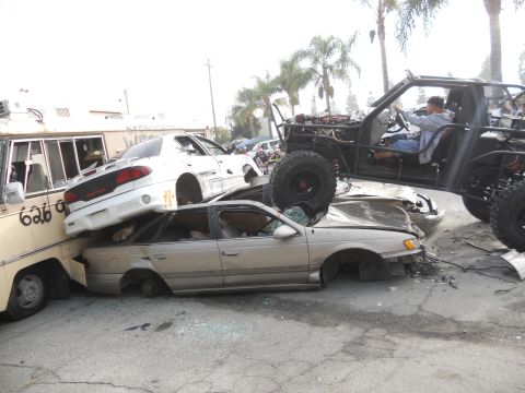1986 Ford Bronco - A custom buggy is perched atop a stack of damaged vehicles in a junkyard setting.