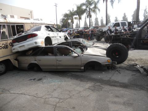1986 Ford Bronco - A chaotic scene of crushed vehicles, with a white sedan precariously balanced atop a tan sedan.