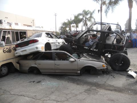 1986 Ford Bronco - A custom-built off-road vehicle is piled on top of several other damaged cars in a junkyard scene.