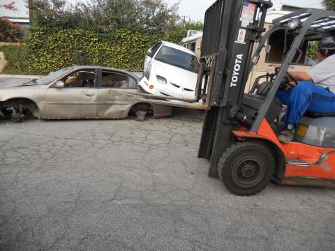 1986 Ford Bronco - A forklift is used to move two heavily damaged cars on a street.