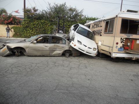 1986 Ford Bronco - Multiple vehicles are severely damaged and piled up on a street.