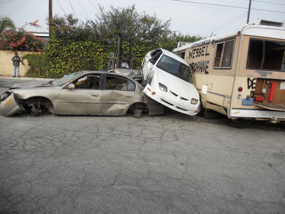 Damaged gold sedan and white car crushed against a propane truck