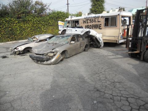1986 Ford Bronco - Multiple wrecked vehicles are visible, including sedans and a propane truck, with a forklift nearby.