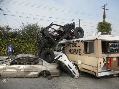 1986 Ford Bronco - A chaotic scene shows multiple vehicles crushed and damaged, with a buggy perched atop a bus.