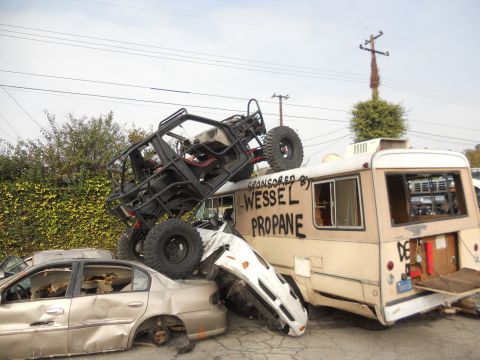 1986 Ford Bronco - A chaotic scene with a buggy perched atop a bus, surrounded by crushed vehicles.
