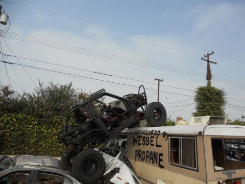 1986 Ford Bronco - An off-road buggy is precariously balanced on a stack of vehicles, including a camper van with 'Wessel Propane' written on its side.
