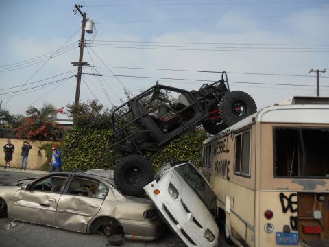 1986 Ford Bronco - A chaotic scene shows an off-road vehicle precariously balanced on a bus, with multiple cars crushed underneath.
