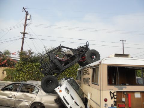 1986 Ford Bronco - An off-road buggy is precariously balanced on an RV, which itself is stacked on damaged cars.