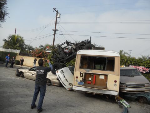 1986 Ford Bronco - A person captures a scene of destruction where several vehicles, including a bus and a buggy, are stacked and damaged on a street.