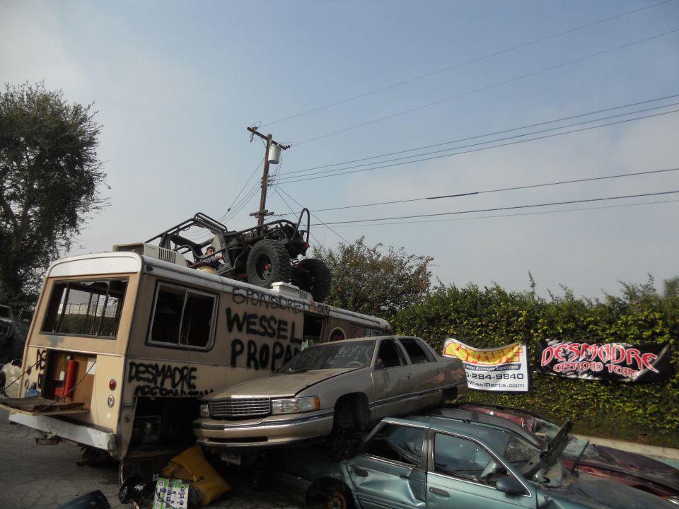 Bus with a buggy on top, and cars stacked around it. Text spray-painted on the bus