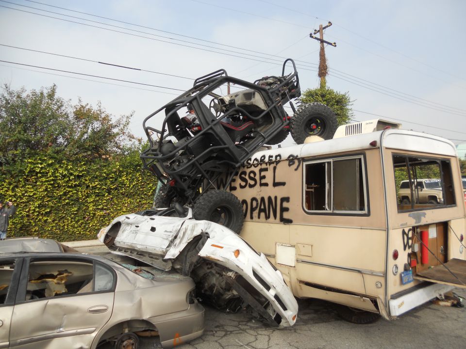Buggy on top of wrecked cars and a bus with 'WESSEL PROPANE' written on it