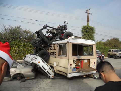 1986 Ford Bronco - A chaotic scene with multiple wrecked vehicles, including a bus and a buggy, piled up in a yard.