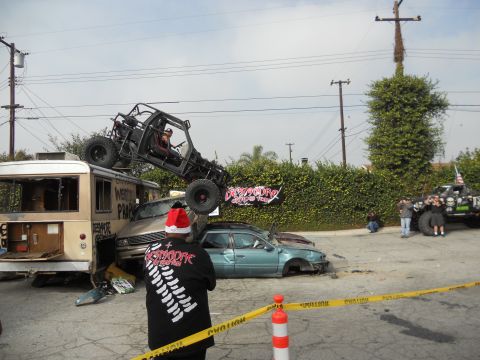 1986 Ford Bronco - A chaotic scene with a buggy precariously balanced on a bus, surrounded by damaged vehicles and onlookers.