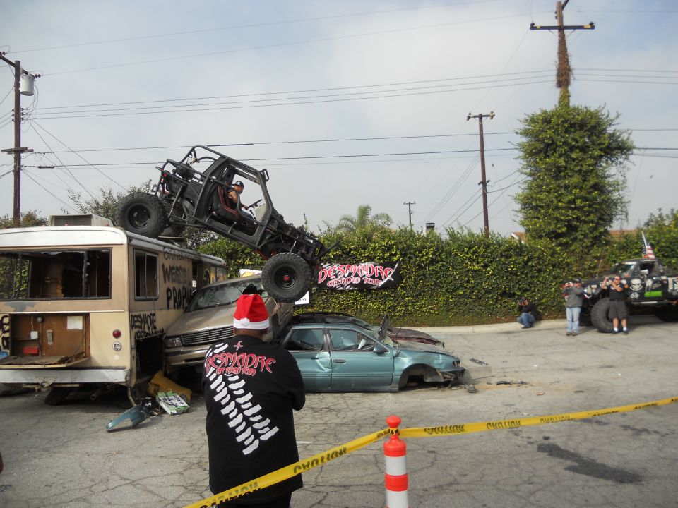 Buggy on top of a bus, with a crushed car nearby. People watching, caution tape up