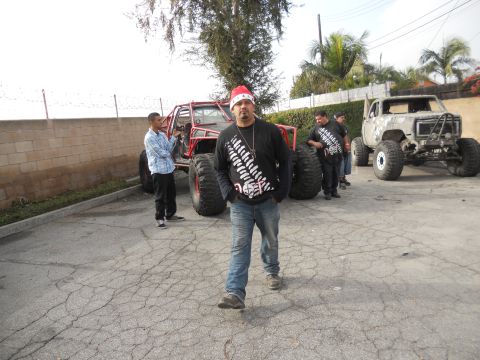 1986 Ford Bronco - Two heavily modified off-road vehicles are parked outside with several people.