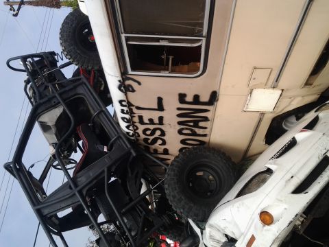 1986 Ford Bronco - An off-road vehicle is precariously balanced on a white car, with graffiti visible on a nearby trailer.