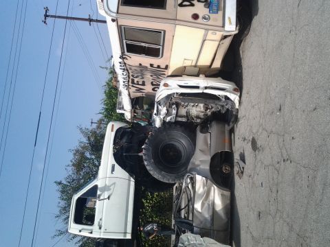 1986 Ford Bronco - A collection of damaged vehicles, including a large truck and a severely crushed car, are shown in a heap on the asphalt.