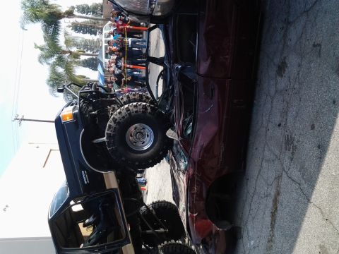 1986 Ford Bronco - A modified 1986 Ford Bronco with off-road tires and a roll cage sits beside a crushed vehicle, possibly at a car crush event.