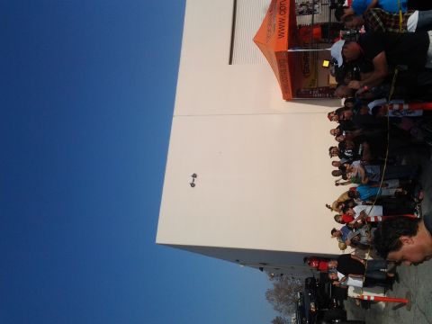 1986 Ford Bronco - A crowd of people are gathered outside a building with an orange tent, under a clear blue sky.