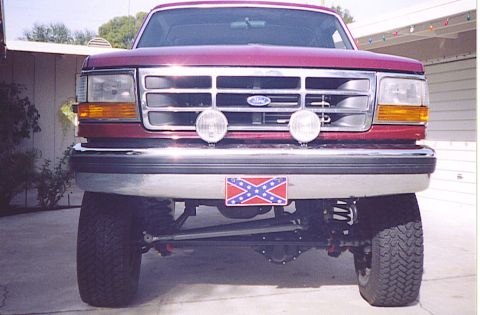 1992 Ford Bronco - This lifted Ford truck features a prominent grille and auxiliary lights, with a distinctive flag on the license plate.