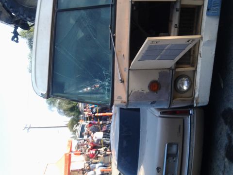1986 Ford Bronco - A damaged bus with a cracked windshield and an open hood is visible, with a crowd of people in the background.