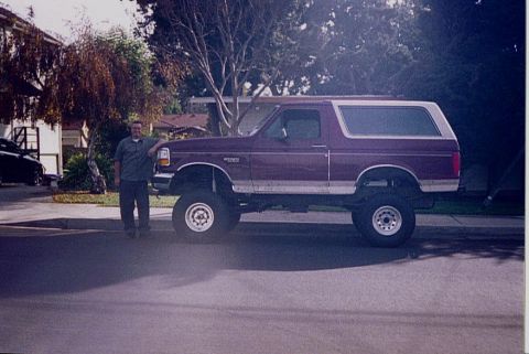 1992 Ford Bronco - A man stands next to a lifted maroon 1992 Ford Bronco with a white top.