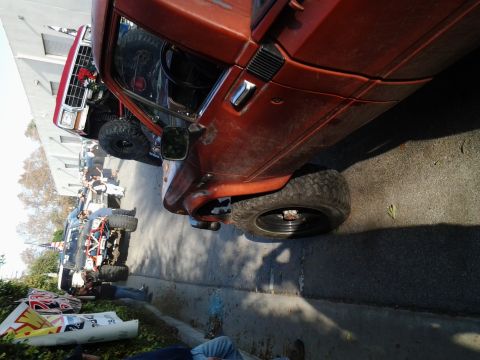 1986 Ford Bronco - Multiple off-road trucks are gathered on a street, with one orange truck prominently featured.