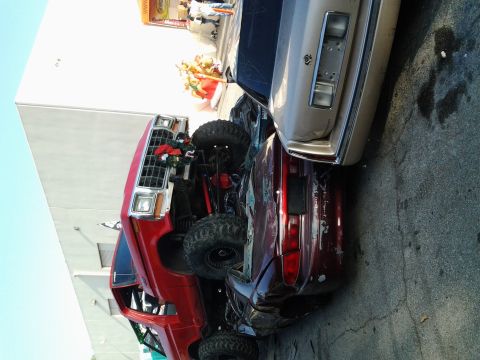 1986 Ford Bronco - A red pickup truck and a tan sedan are parked together, with the truck's front end decorated for the holidays.