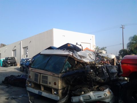 1986 Ford Bronco - Multiple vehicles are piled up in a junkyard scene, with a van prominently in the foreground.