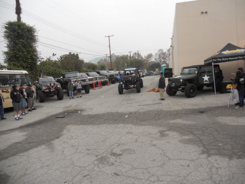 1986 Ford Bronco - A collection of modified off-road vehicles are gathered in a parking lot, with a tent set up in the background.